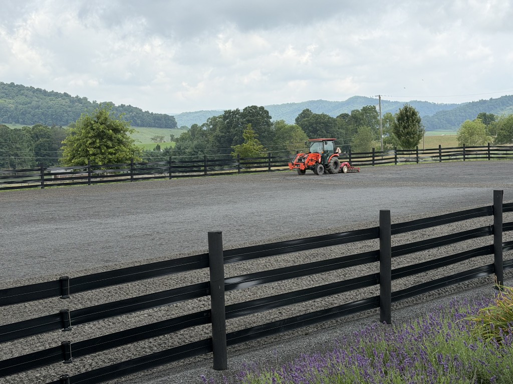 Outdoor riding arena with tractor grooming the footing
